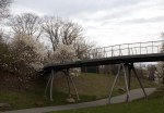 Pedestrian bridge over a park path, surrounded by blooming trees under a cloudy sky